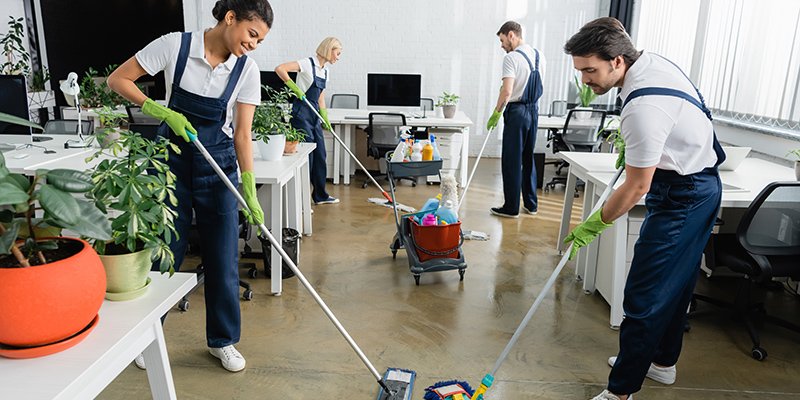 african american cleaner smiling while washing floor near collea